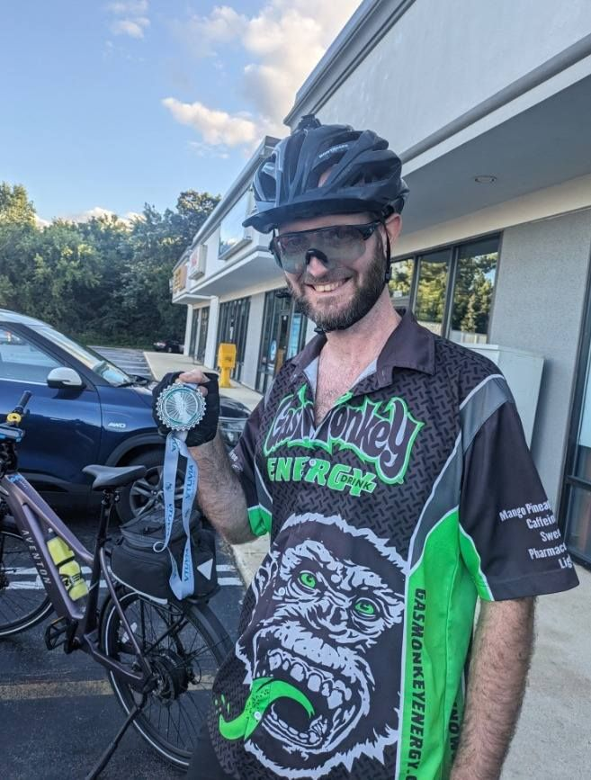 Cyclist in black-and-green jersey and helmet holding a bike light outside a storefront