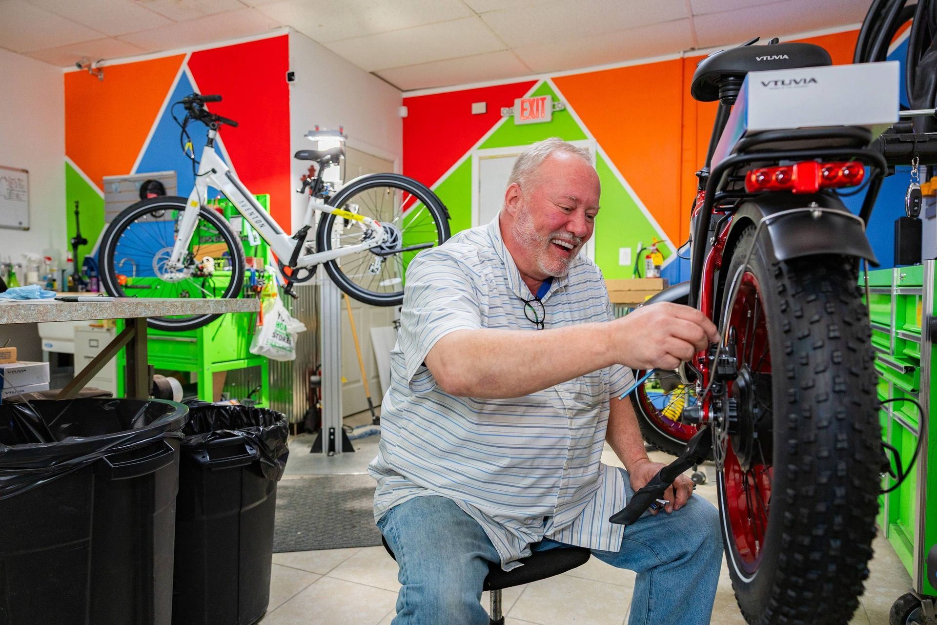 Mechanic repairing a red motorcycle in a colorful bike shop, smiling while working on the rear wheel