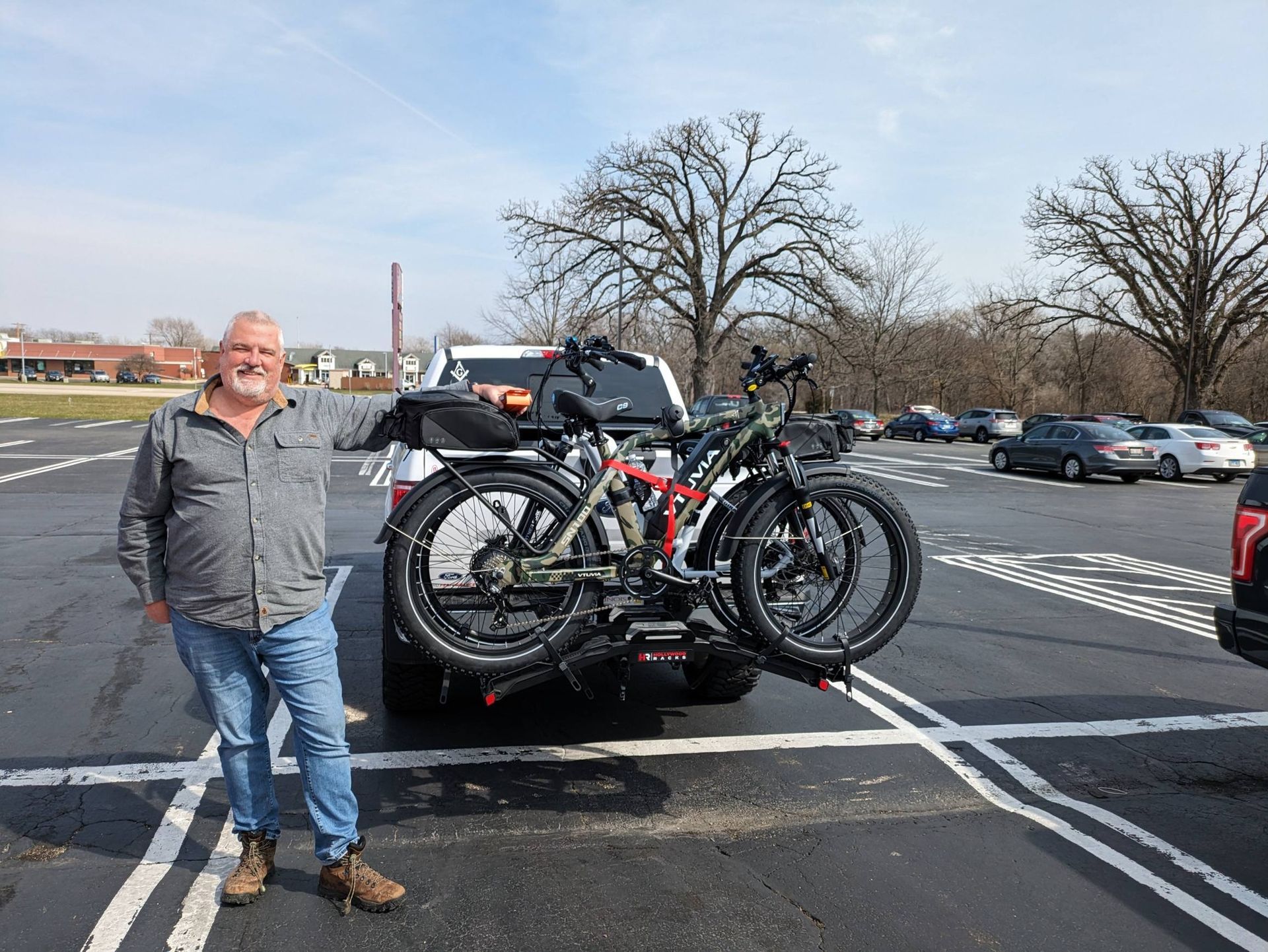 Man smiling beside a car rack loaded with two bicycles in a parking lot