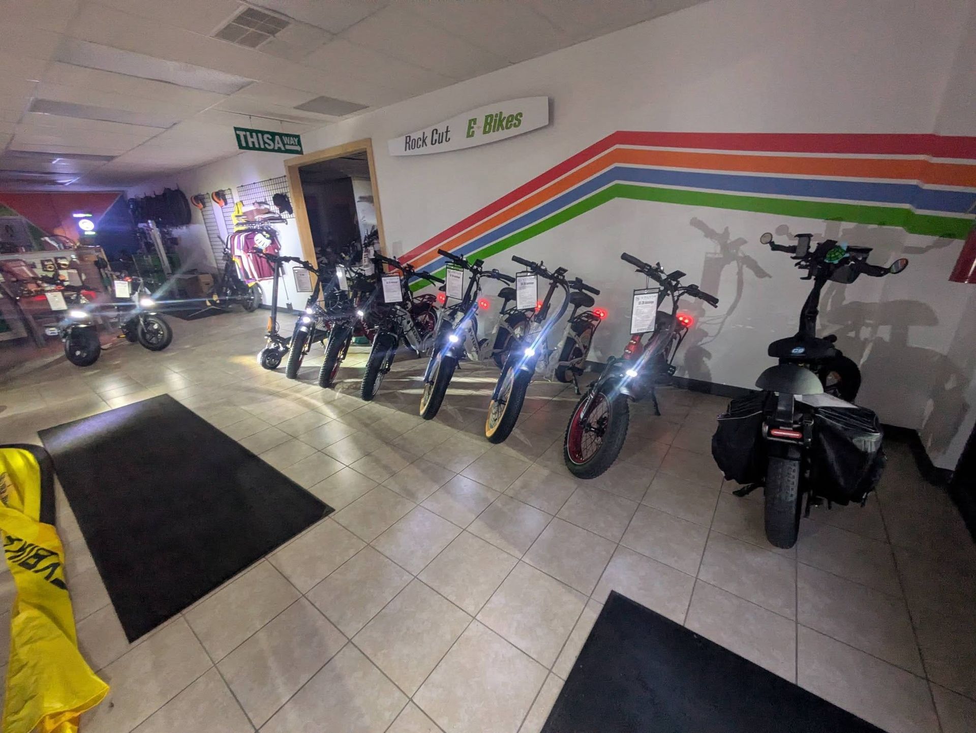 Rows of electric scooters parked indoors beside a wall with colorful stripes and signs.