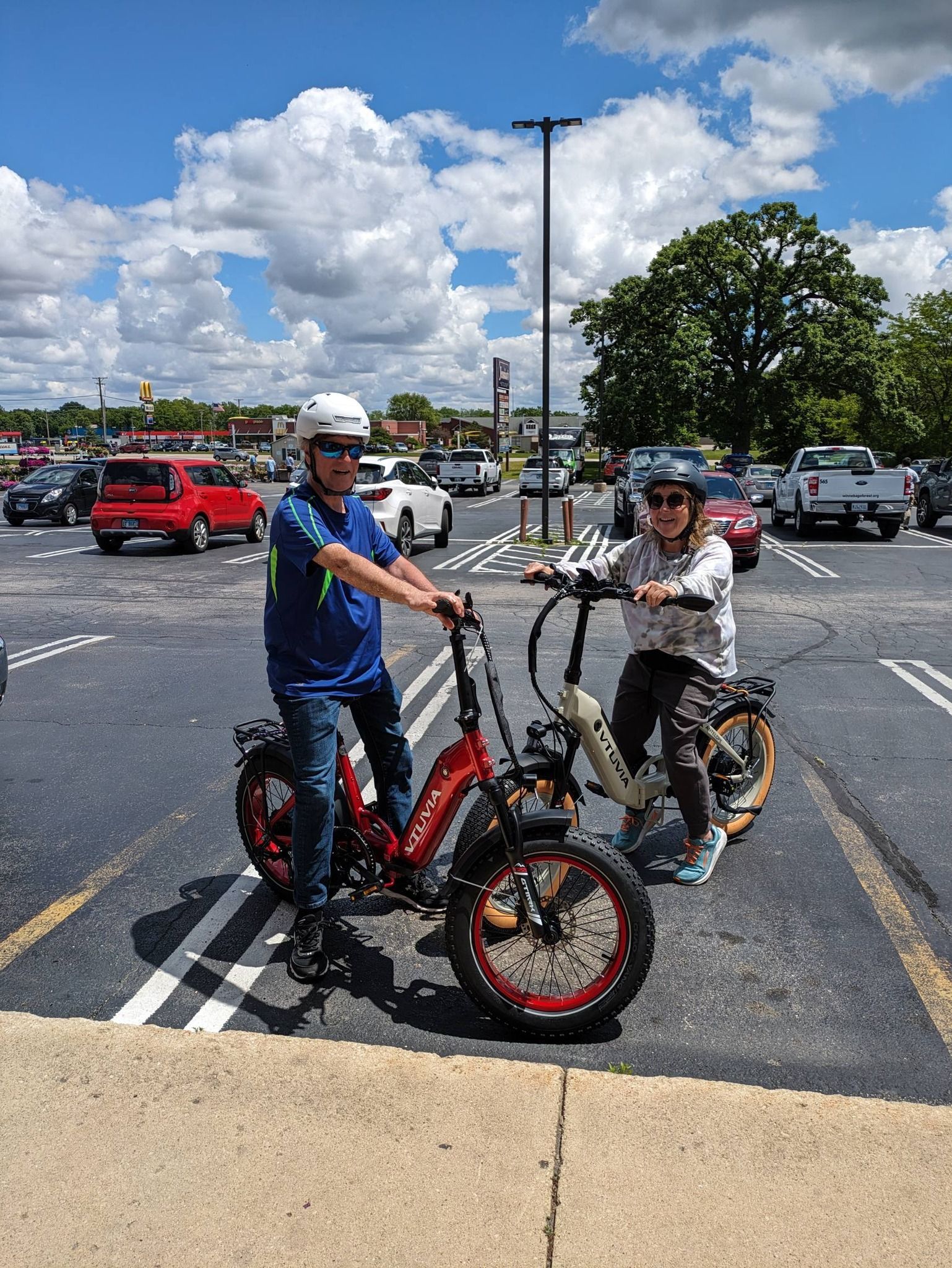 Two cyclists with fat-tire bikes standing in a parking lot on a sunny day