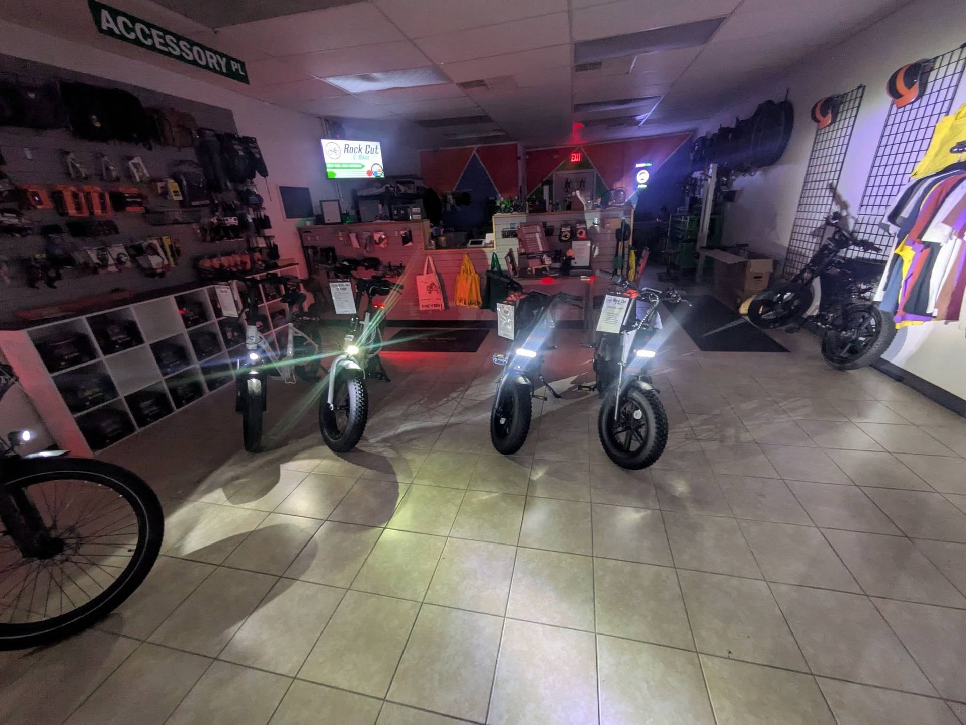 Electric scooters displayed in a showroom with bright headlights on a tiled floor.