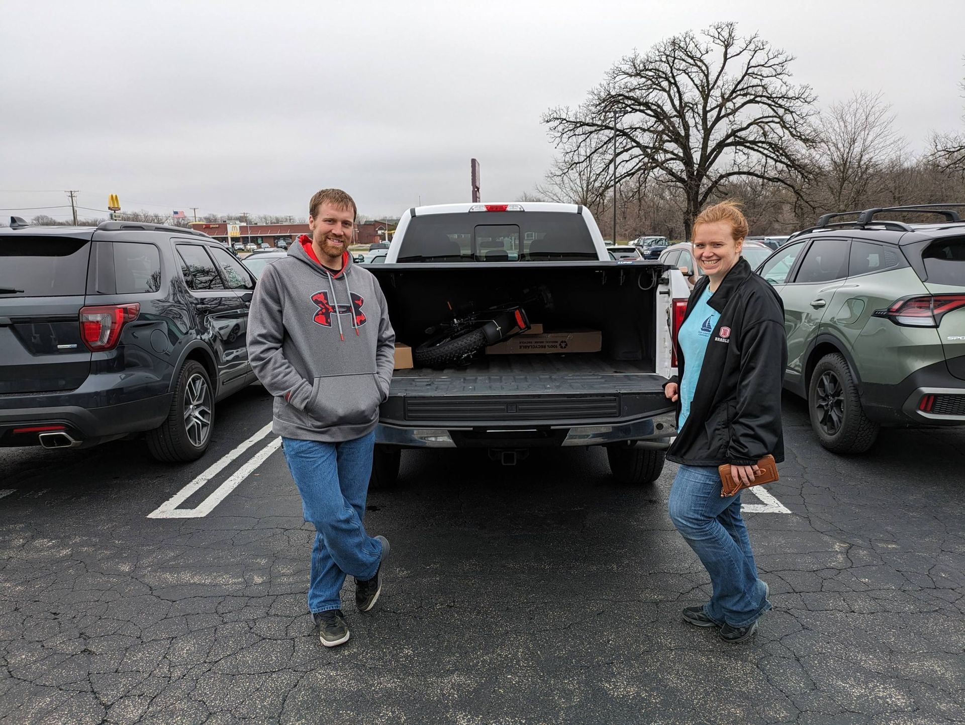 Two people standing behind an open pickup truck in a parking lot on a cloudy day