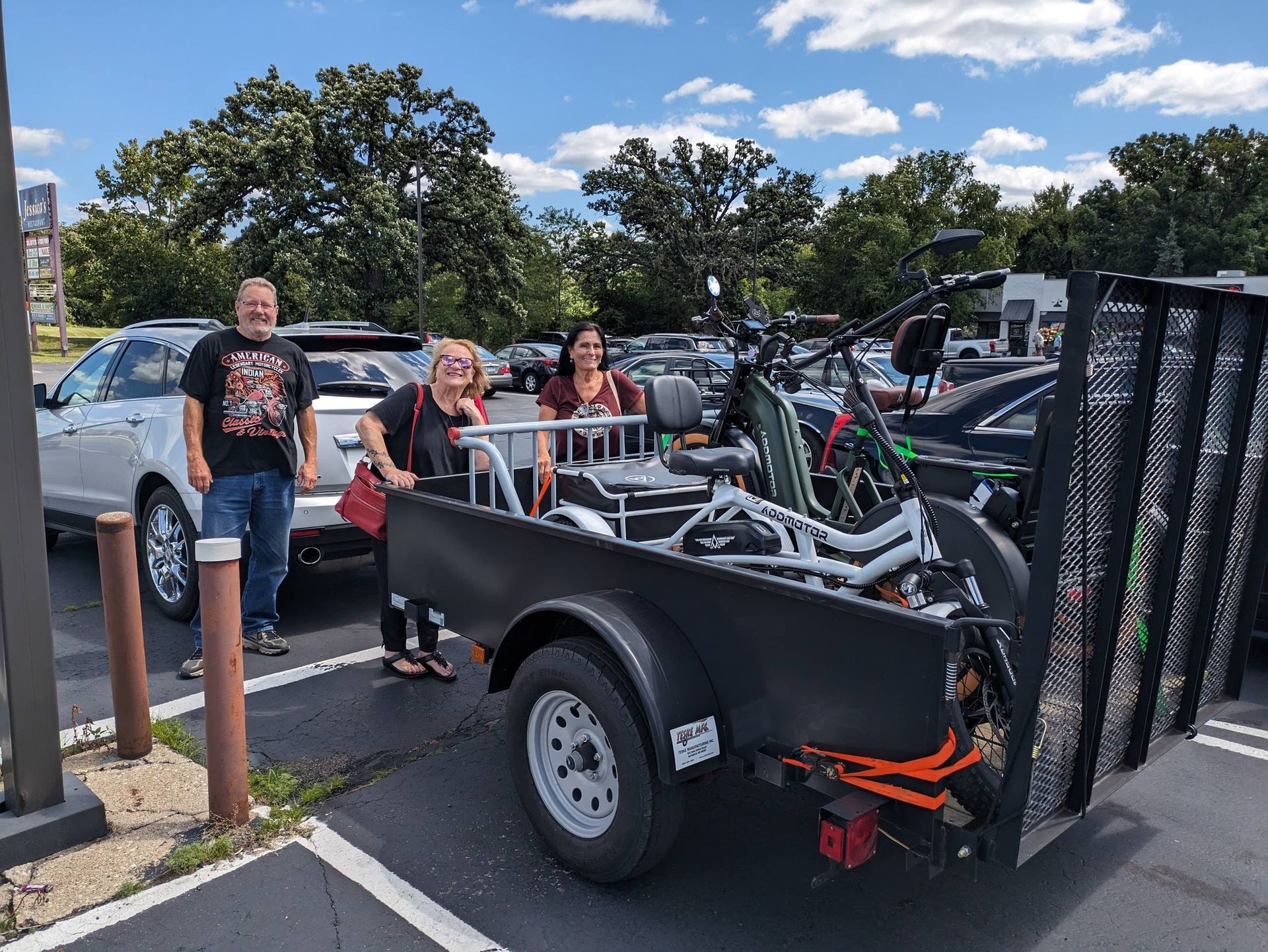 People posing beside a black utility trailer loaded with bicycles in a parking lot
