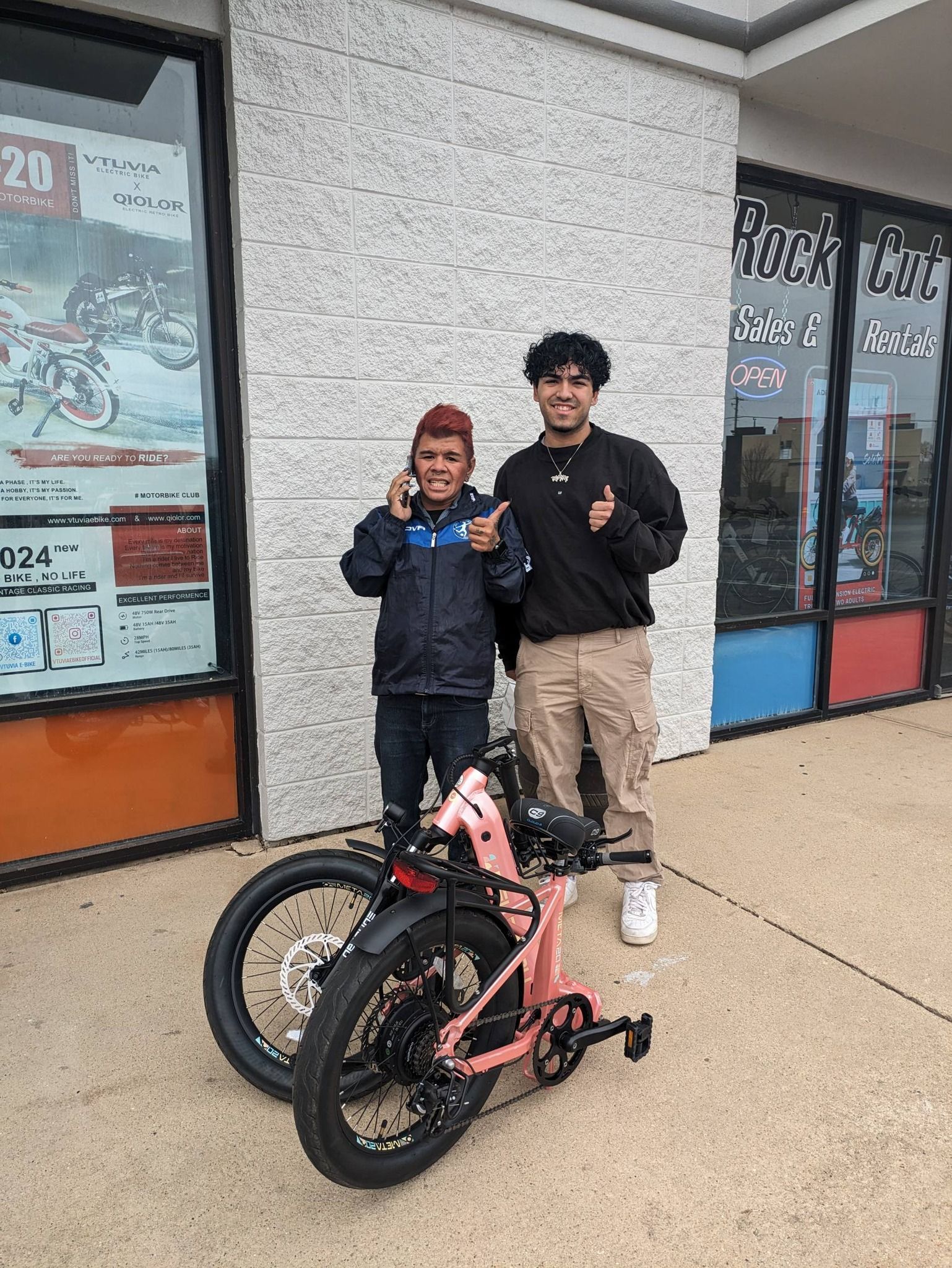 Two people posing beside a pink bicycle outside a storefront
