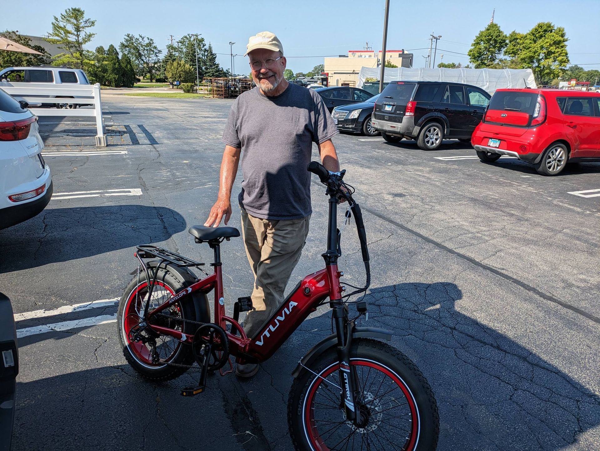 Man standing beside a red folding bicycle in a parking lot, holding the handlebars.