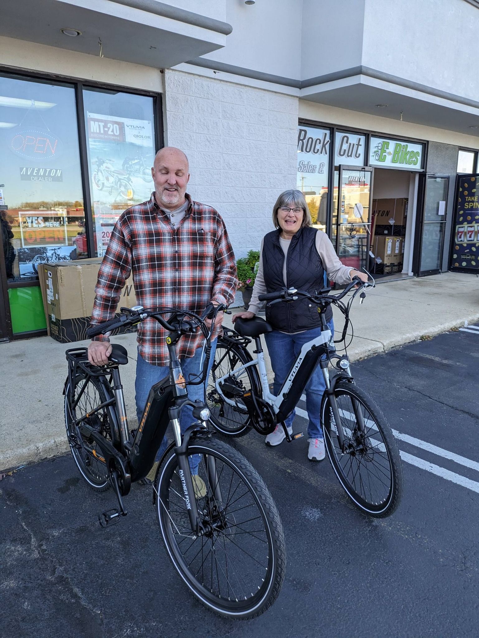 Two people standing with bicycles outside a storefront on a sunny day