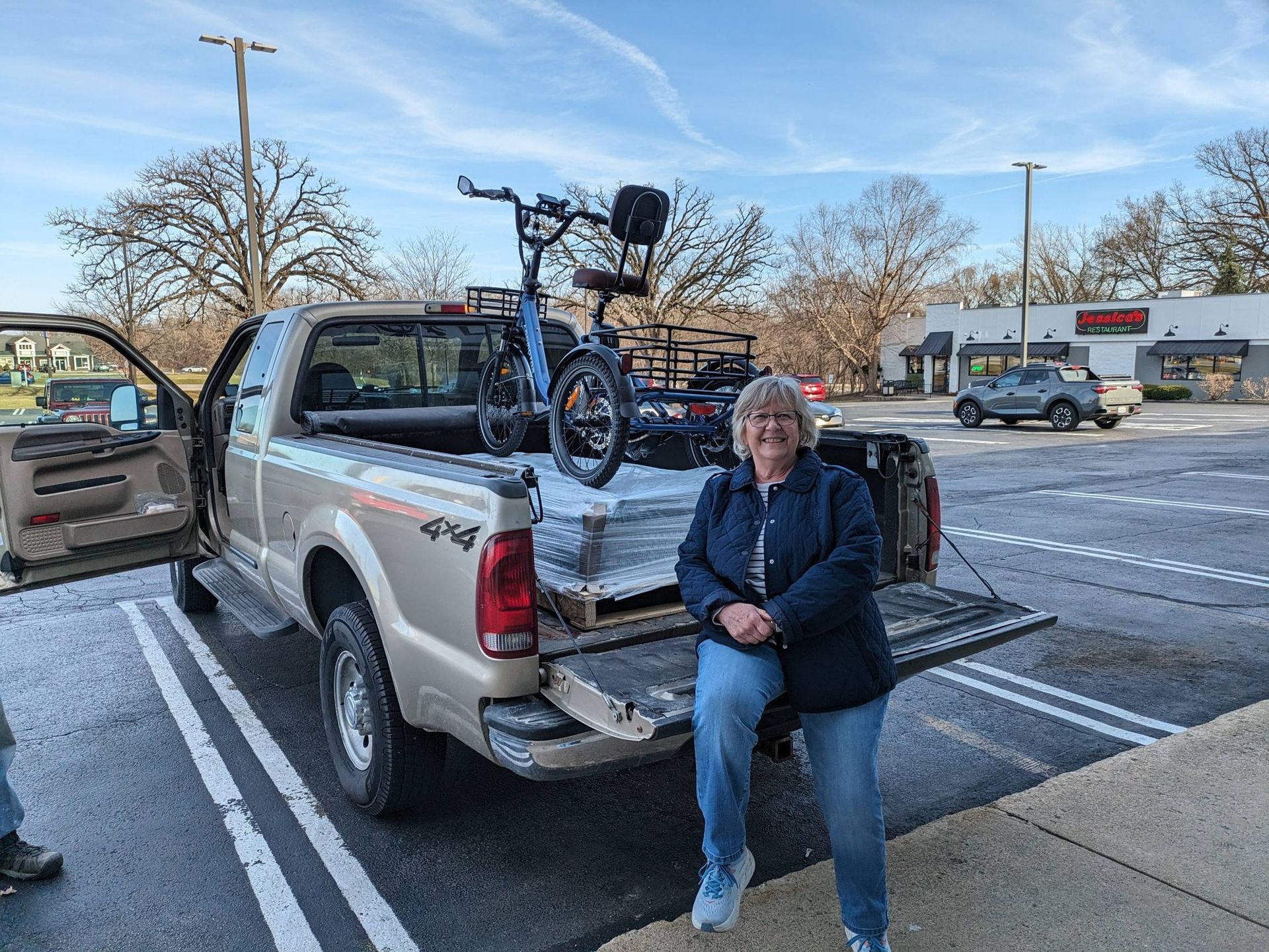 Person sitting on the tailgate of a pickup truck with a bicycle in the bed, parked in a snowy lot.
