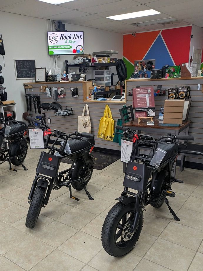 Indoor showroom with several black minibikes displayed on the floor and shelves in the background.
