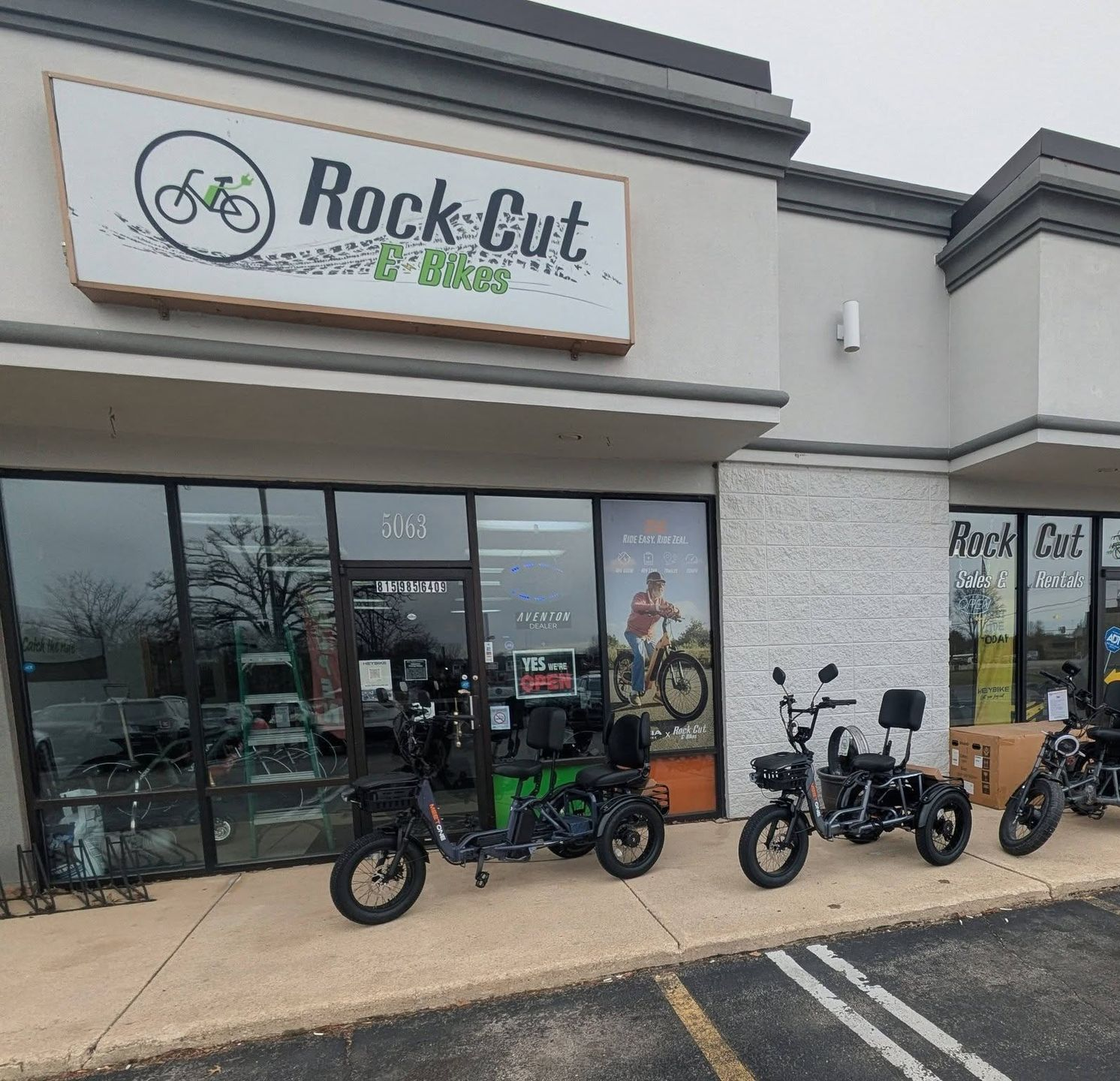 Rock Cut Cycling storefront with several electric bikes parked outside under an overcast sky