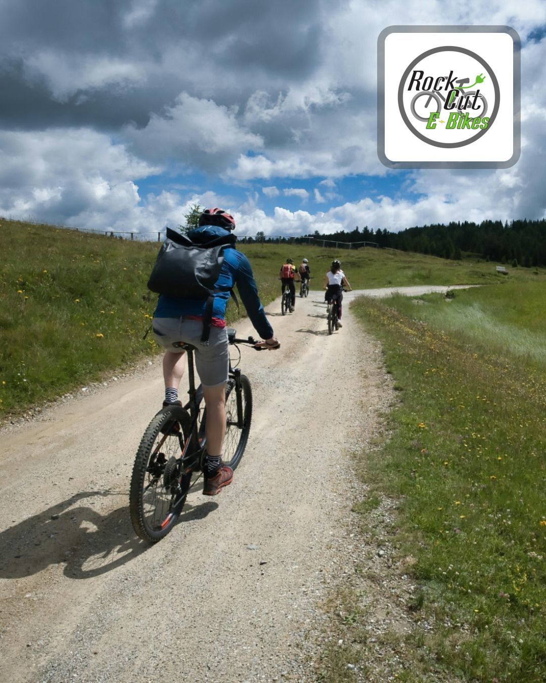 Cyclists ride a gravel path through green hills under a cloudy sky, with one rider in the foreground.