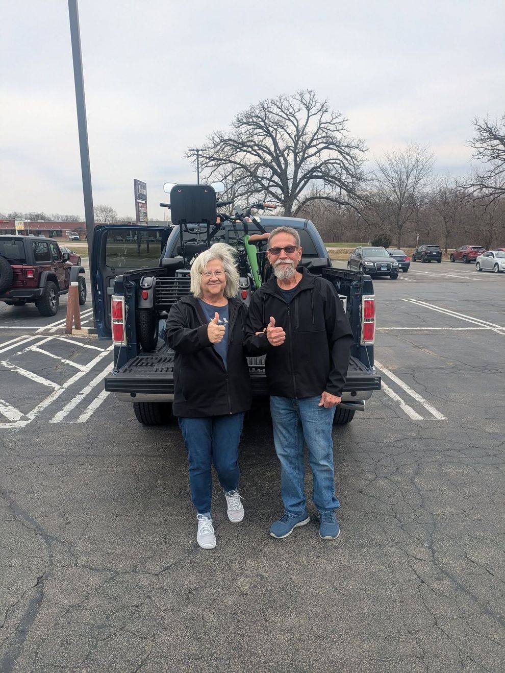 Two people standing in a parking lot, smiling and holding drinks near a truck with cargo equipment.