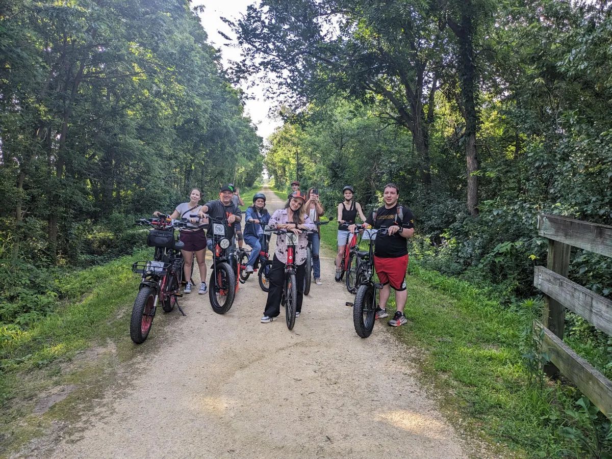 Group of cyclists with bikes on a wooded trail, facing the camera.