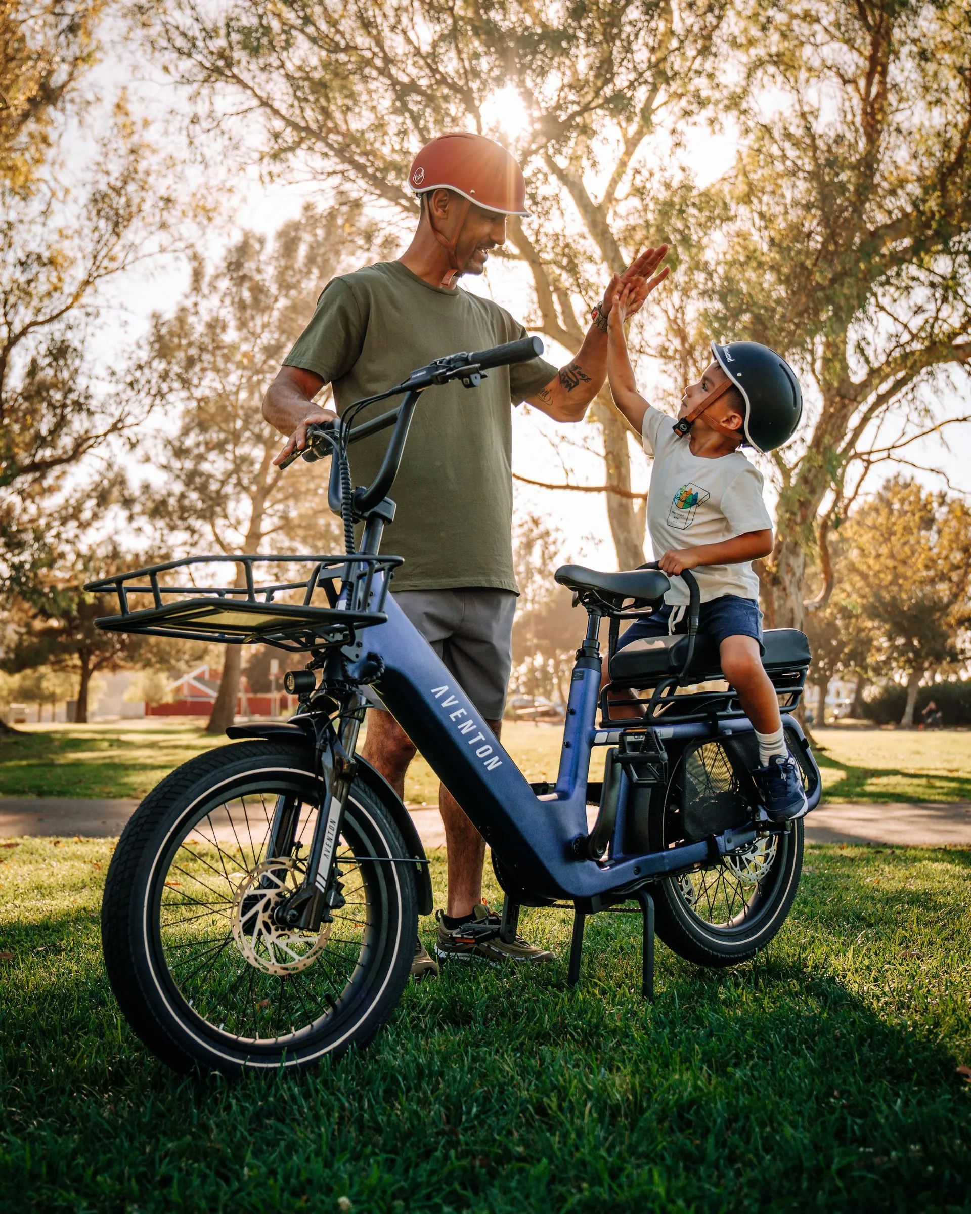 Adult and child high-five beside a black bicycle in a sunny park