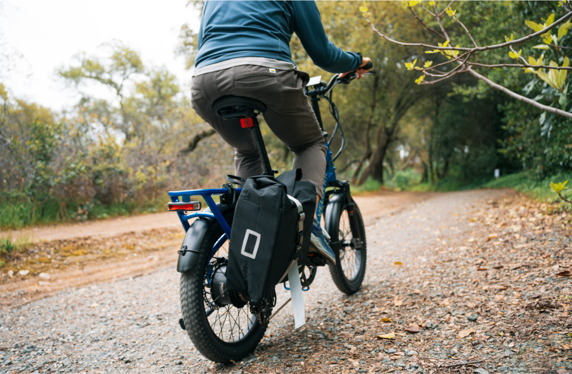 Cyclist riding a blue bike on a gravel path through a wooded park.