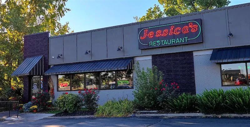 Exterior of a restaurant at dusk with a neon sign, awning, windows, and landscaped shrubs
