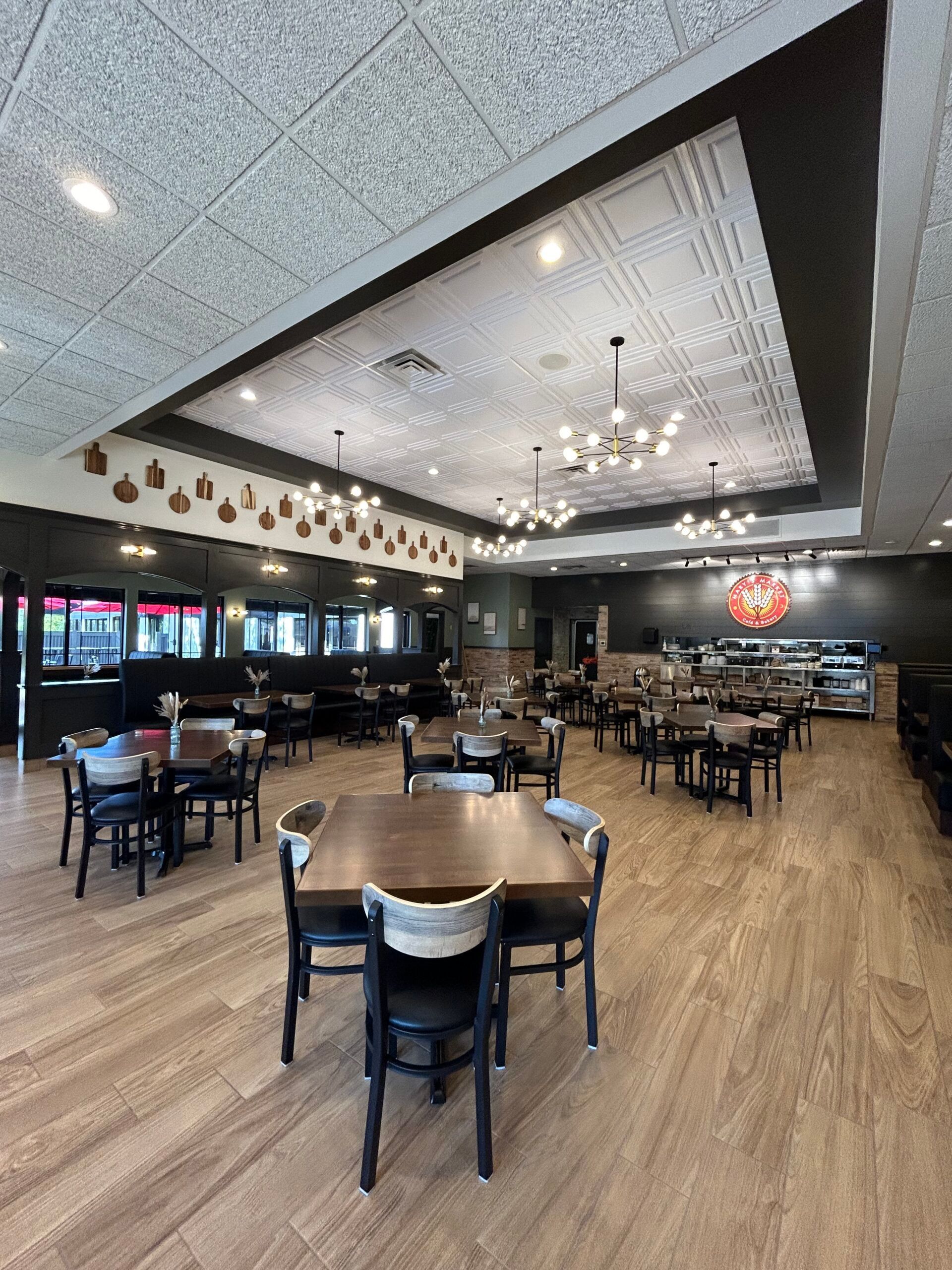 Empty restaurant dining room with black chairs, wooden tables, and warm lighting under a vaulted ceiling