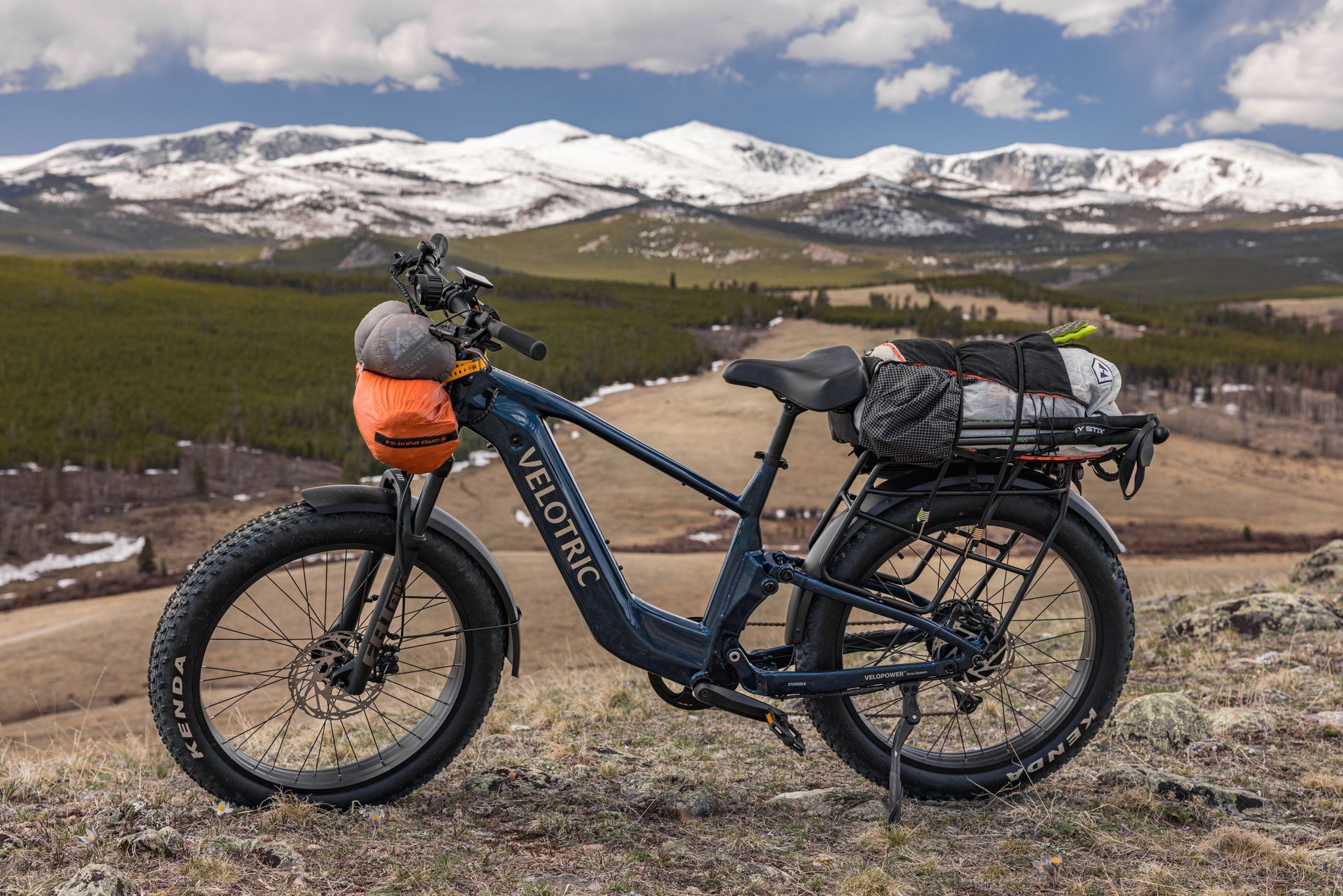 Blue bike with orange bags parked on a rocky overlook with mountains and a valley in the background