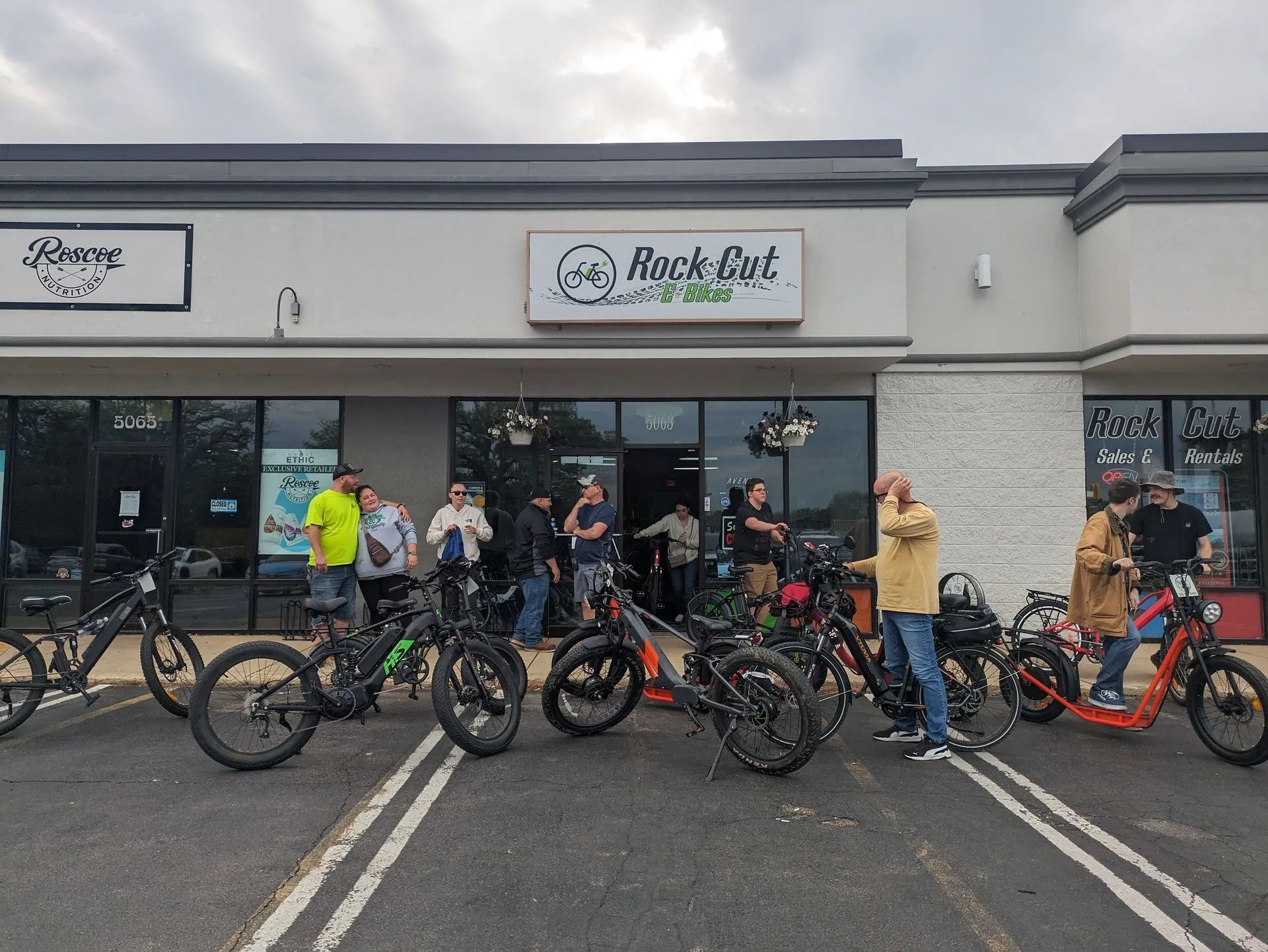 Group of cyclists with bikes outside a bike shop in a parking lot