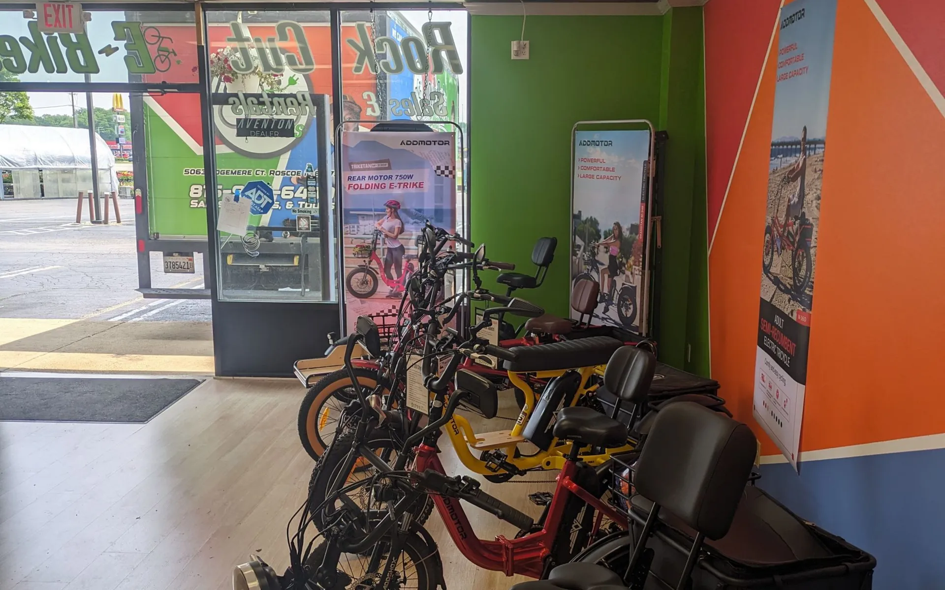 Bicycles lined up outside a storefront with green and orange walls and glass doors.