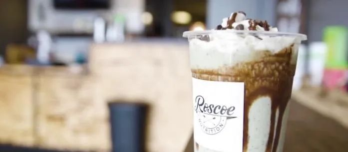 Iced coffee topped with whipped cream in a branded plastic cup on a counter, café background blurred