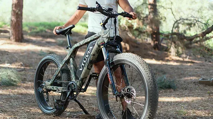 Mountain bike with a rider standing on a dirt trail in a wooded area
