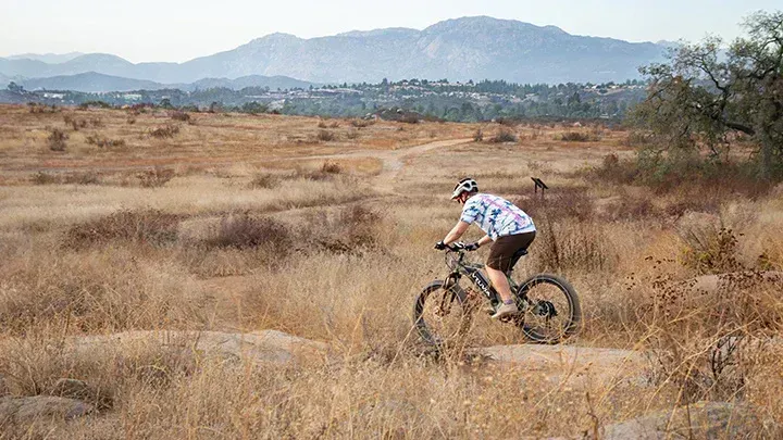 Cyclist riding through a dry grassy field with mountains in the background