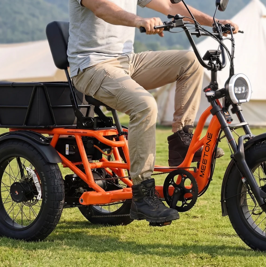 Person riding an orange cargo tricycle on grass outdoors