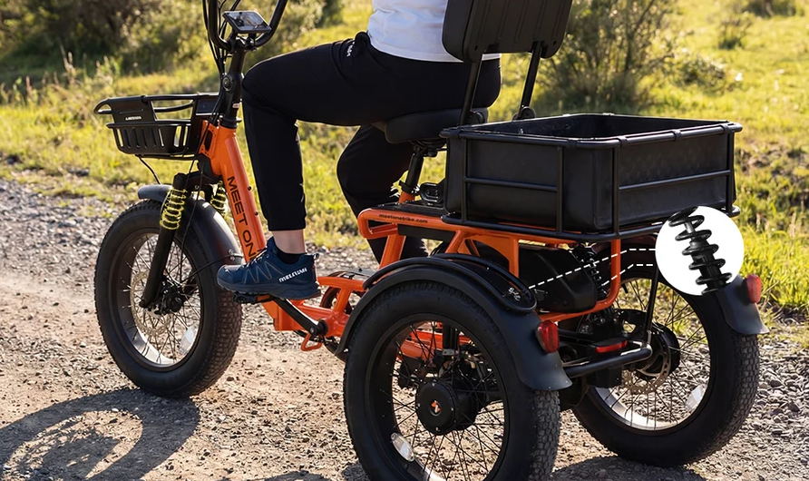 Person riding an orange fat-tire electric bike on a dirt path, with a black cargo box on the back