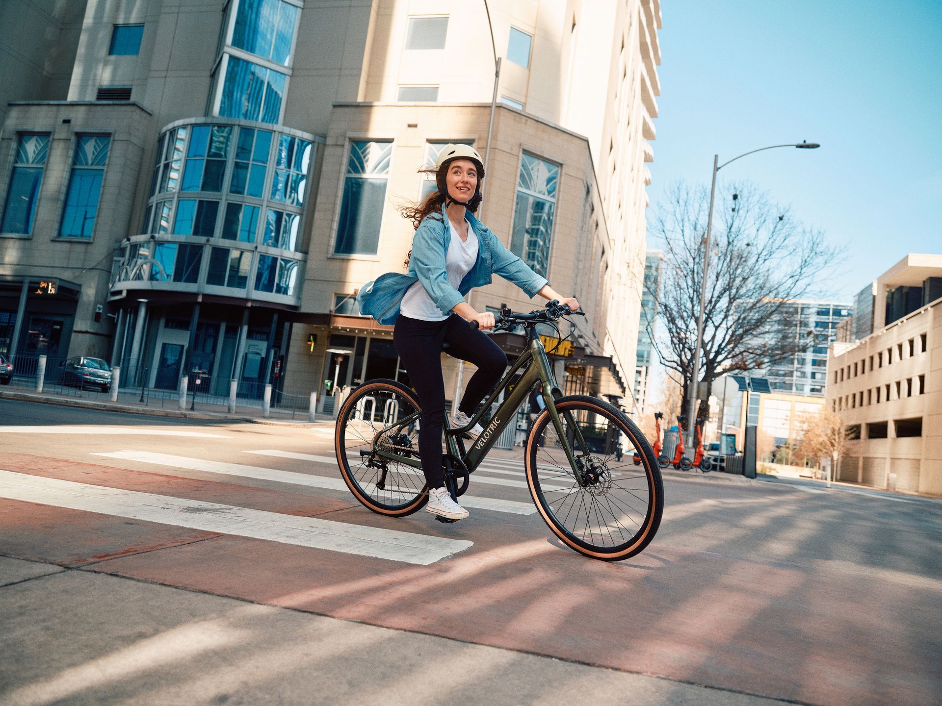 Cyclist riding a bike across a city crosswalk past modern buildings on a sunny day