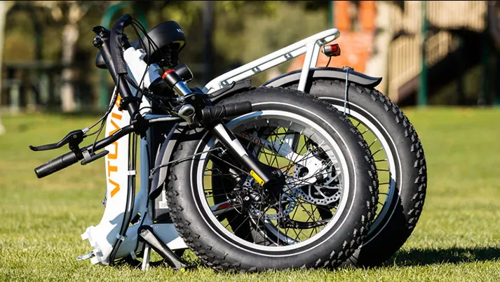 Folded electric bikes parked on grass outdoors, showing large wheels and white frames.