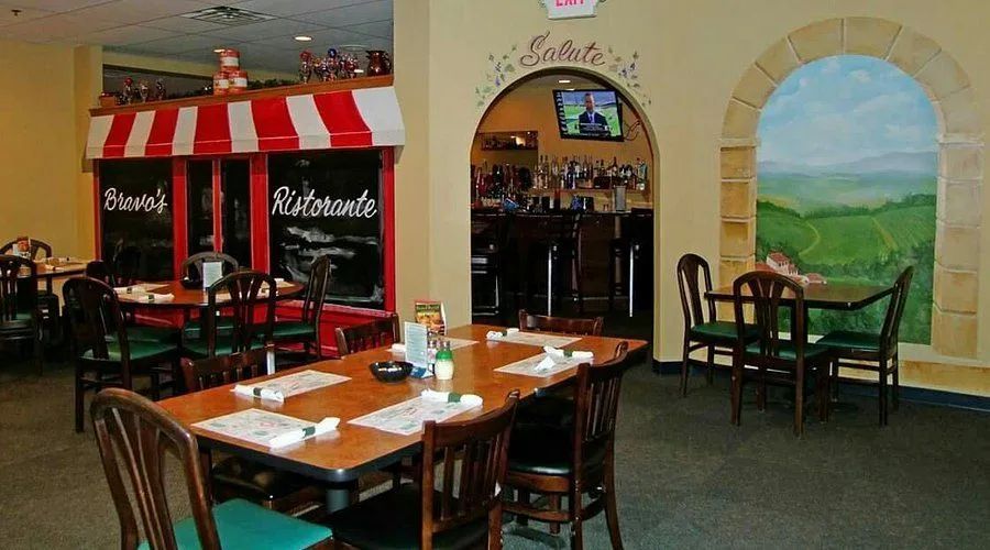 Empty restaurant dining area with wooden tables, chairs, and red-and-white striped awning.