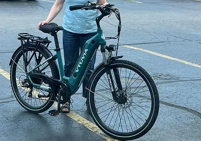 Person standing with a teal electric bicycle on a wet street.
