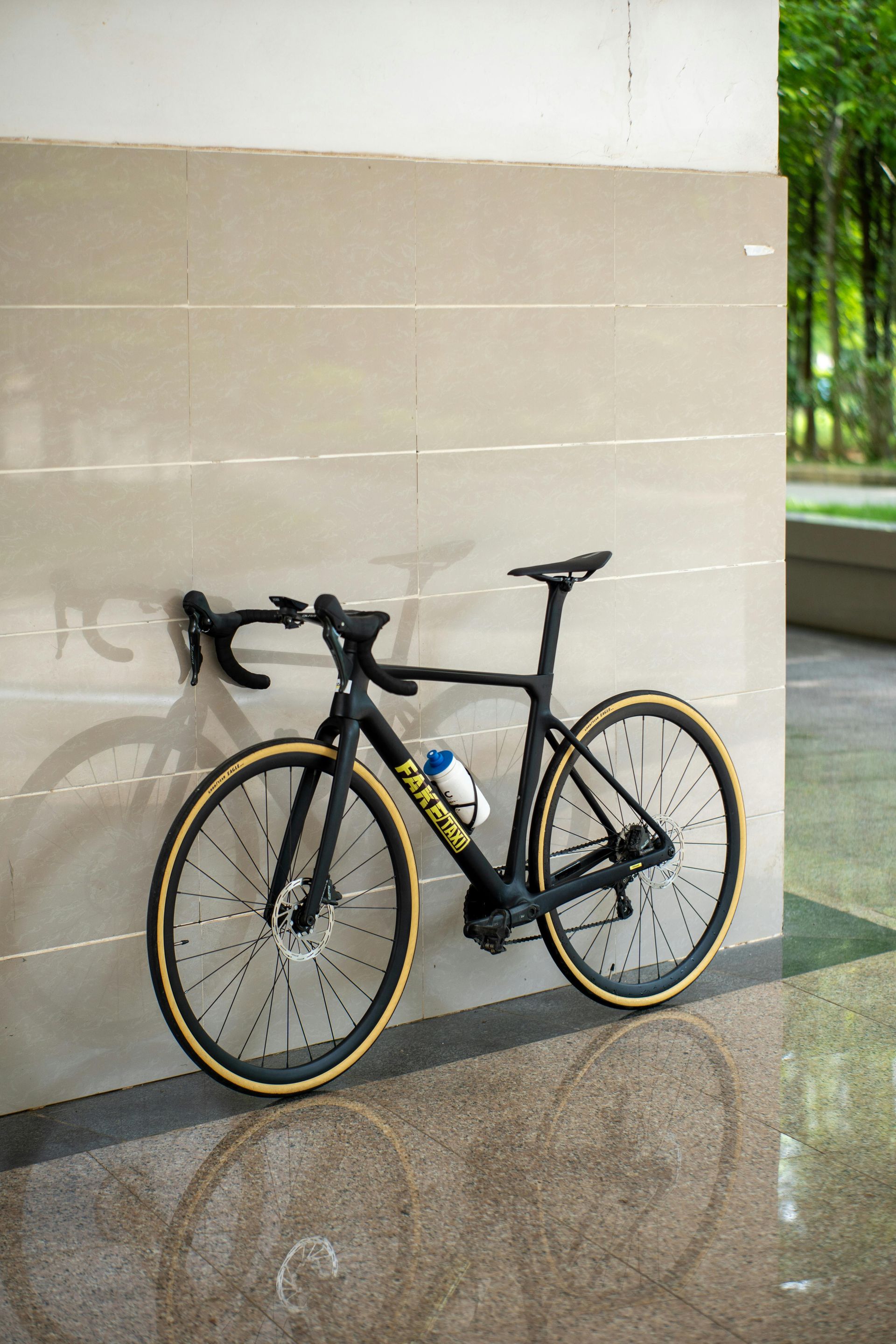 Black road bike leaning against a beige wall on a tiled floor.