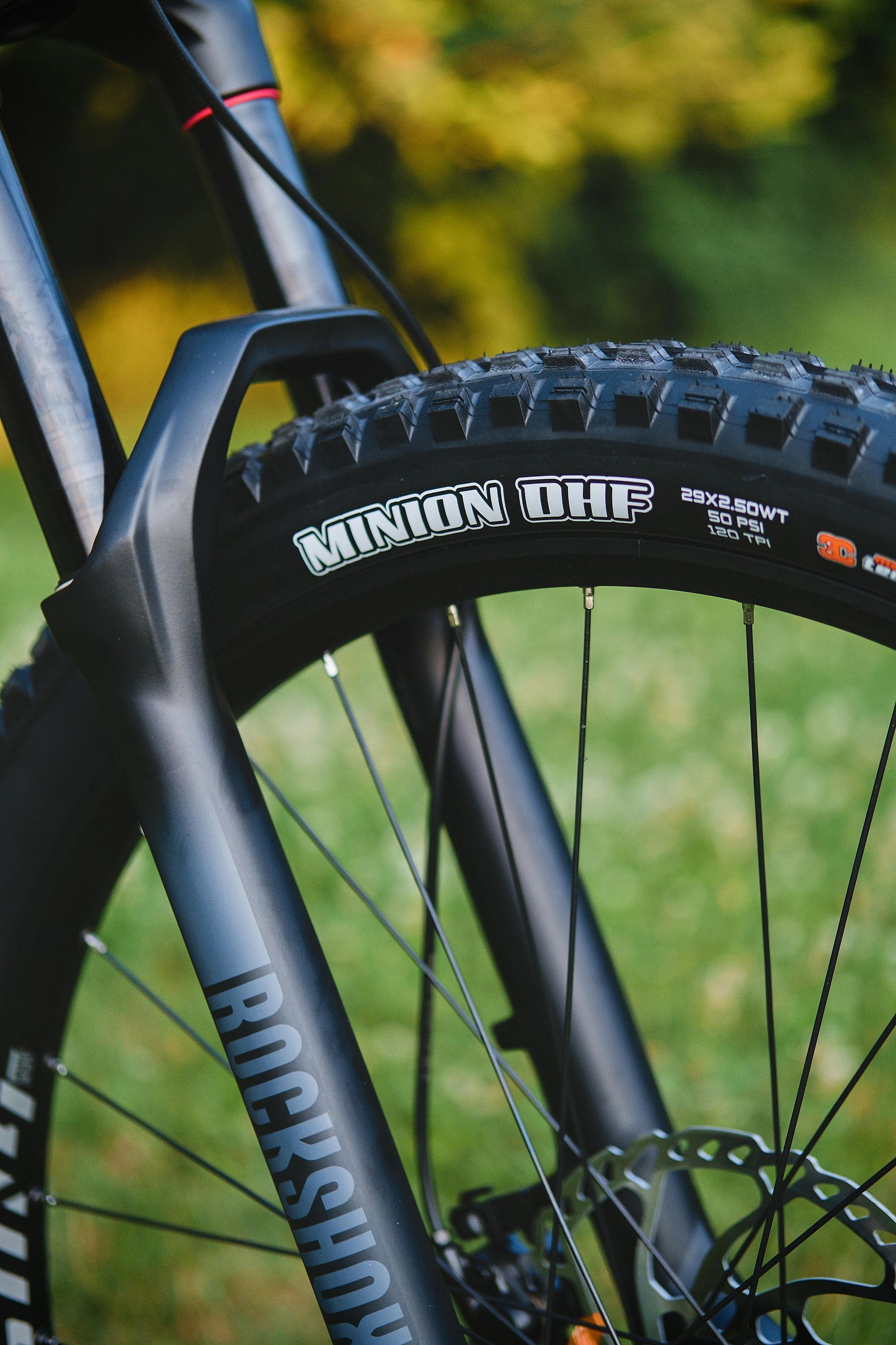 Close-up of a mountain bike wheel and fork on a grassy trail.