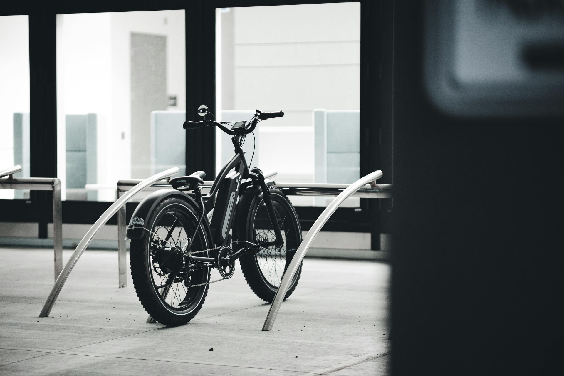 Black bicycle parked beside curved metal racks outside a modern building.