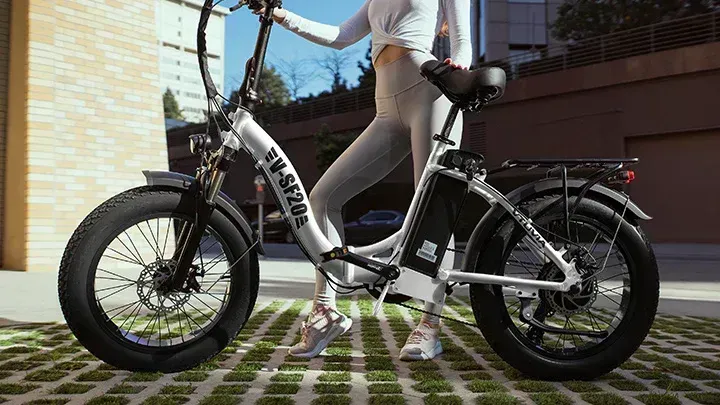 Person standing beside a white electric fat-tire bike on a paved path outdoors