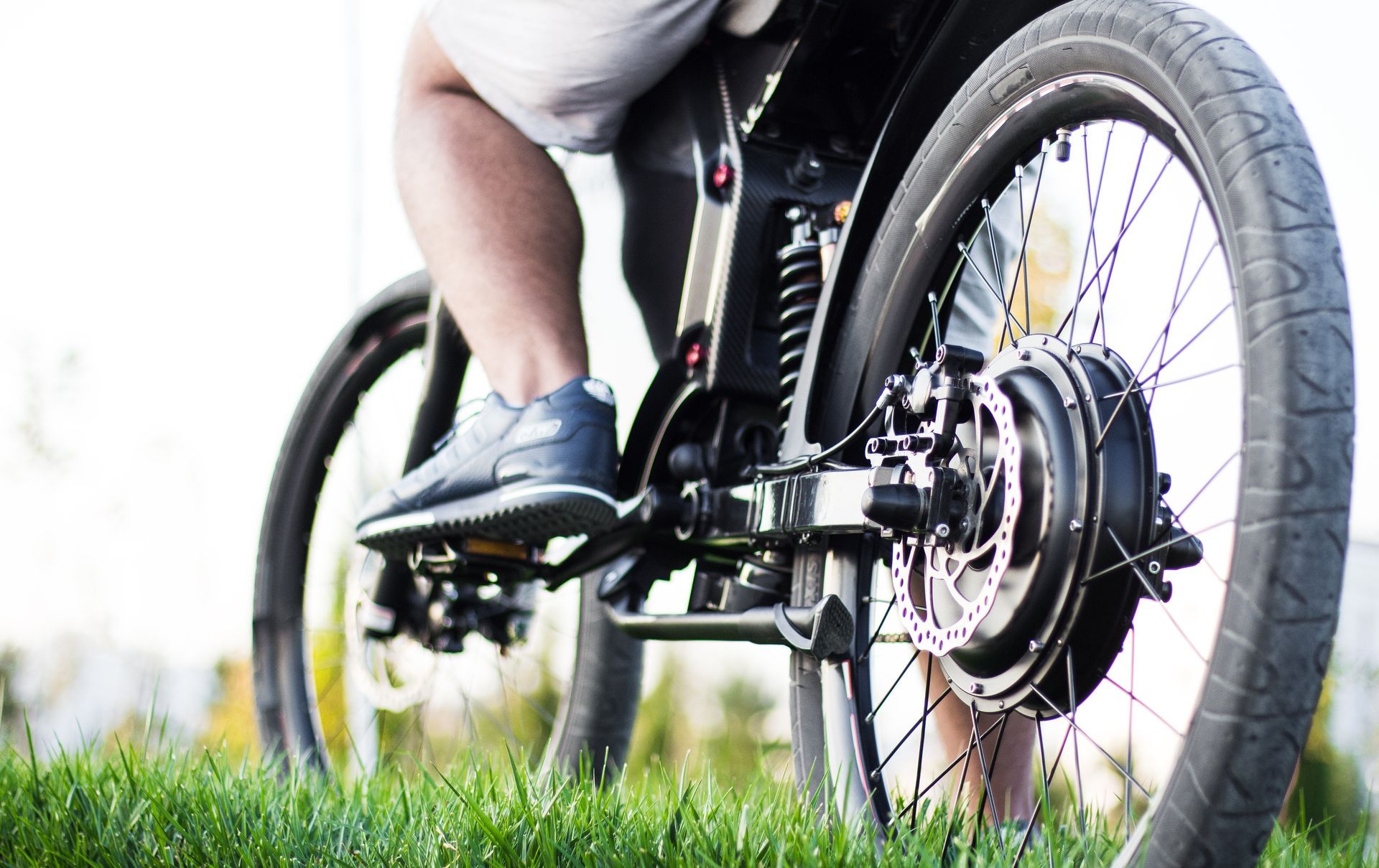 Person riding a bicycle on grass, close-up of the pedals and rear wheel