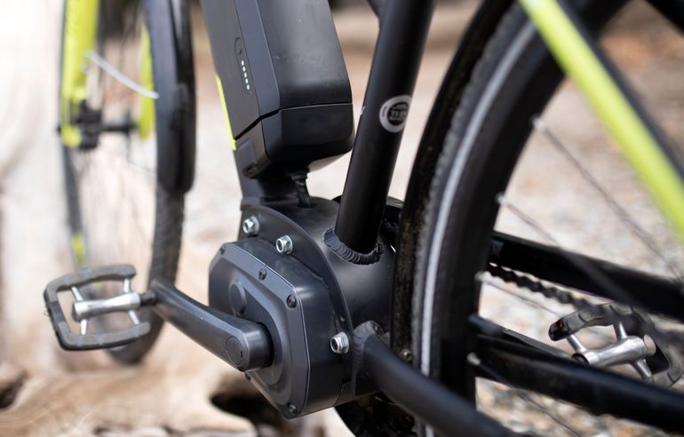 Close-up of an electric bicycle's mid-drive motor and pedal near a rear wheel.