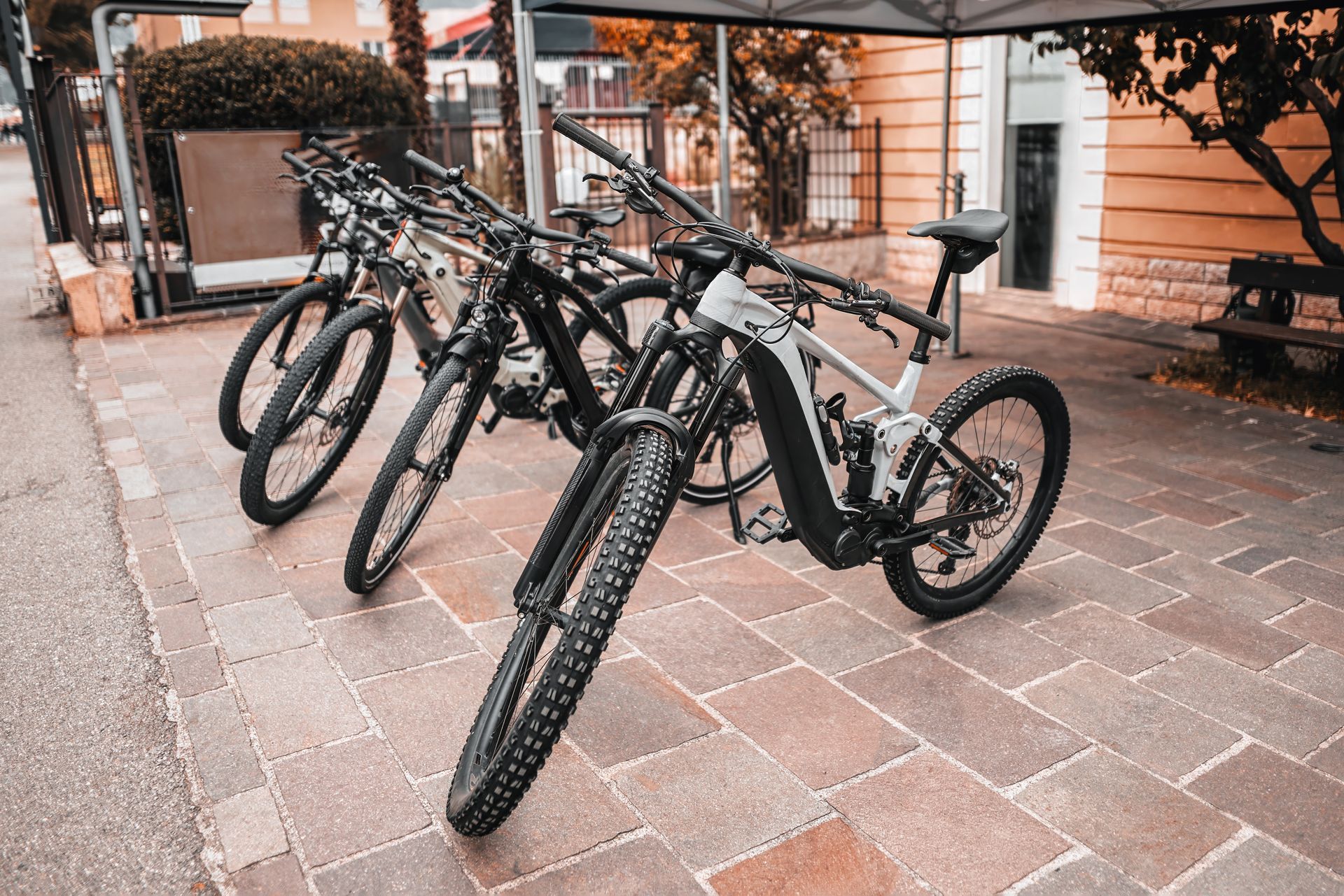 Several black mountain bikes parked on a brick patio near a building