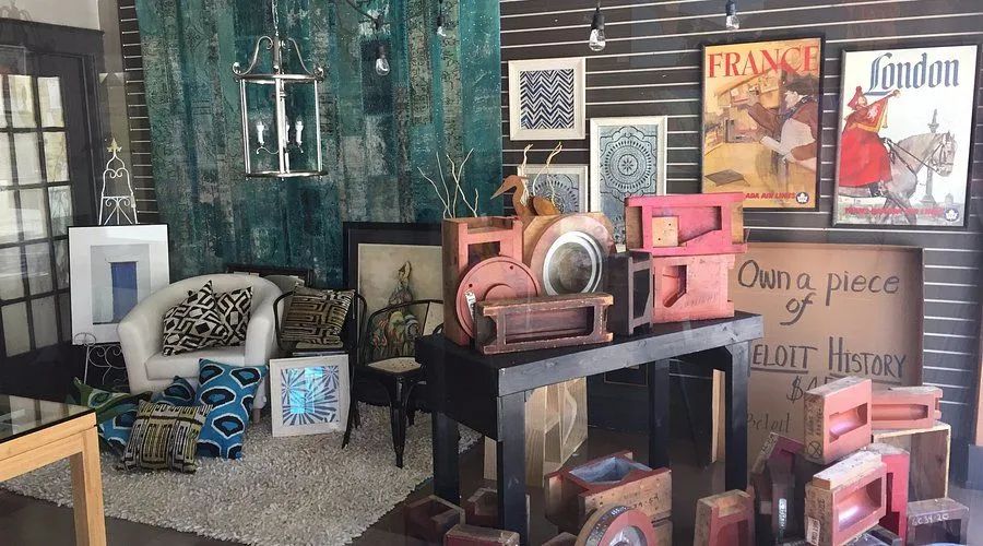 Vintage-style room display with pink and black furniture, framed art, and decorative signs on a patterned wall.