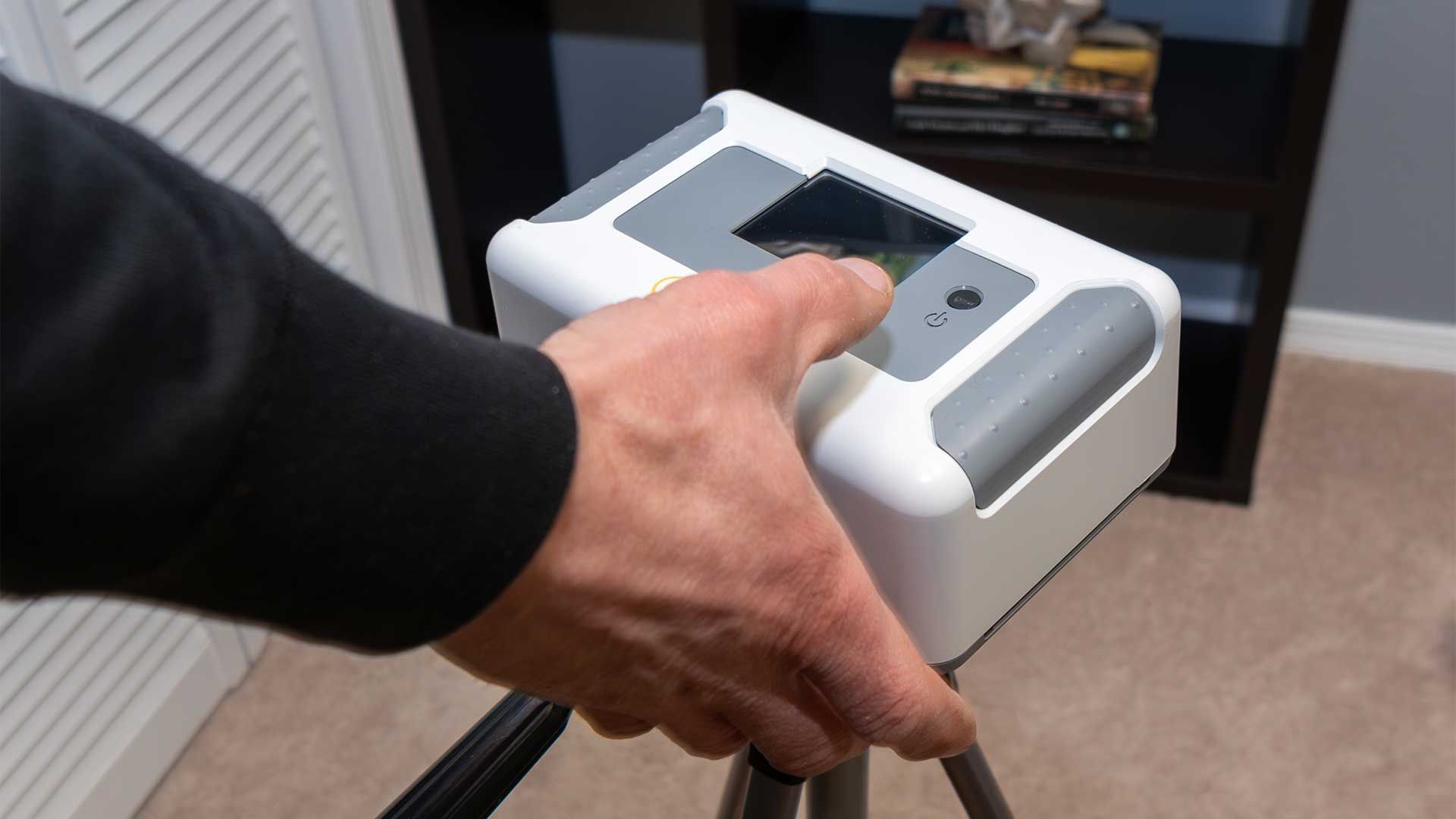 A person is holding a white device on a tripod.