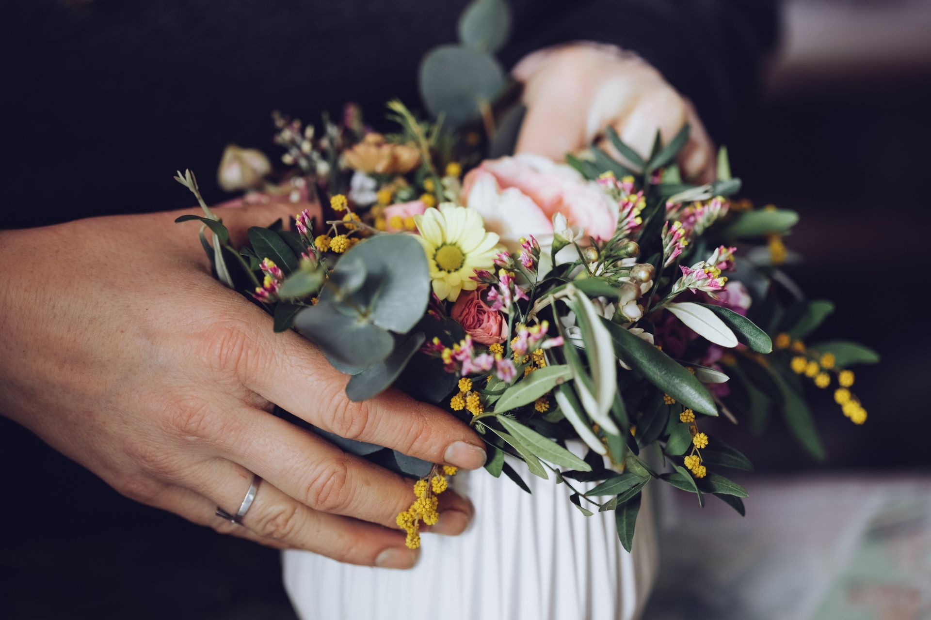 Mani che sistemano un piccolo bouquet di fiori rosa, gialli e bianchi legati con un nastro