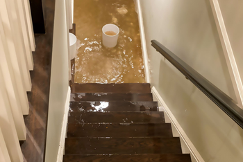 Water Damage | Watervliet, MI | Mr. Cleans Restoration Flooded hallway with water covering the floor and stairs. Buckets are visible. Handrail along stairs.