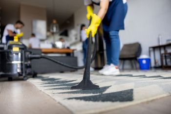 Carpet Cleaning | Watervliet, MI | Mr. Cleans Restoration Person vacuuming a patterned rug in a bright, modern room; others in the background.