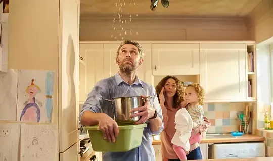 Man catching water in kitchen from ceiling leak, with family.