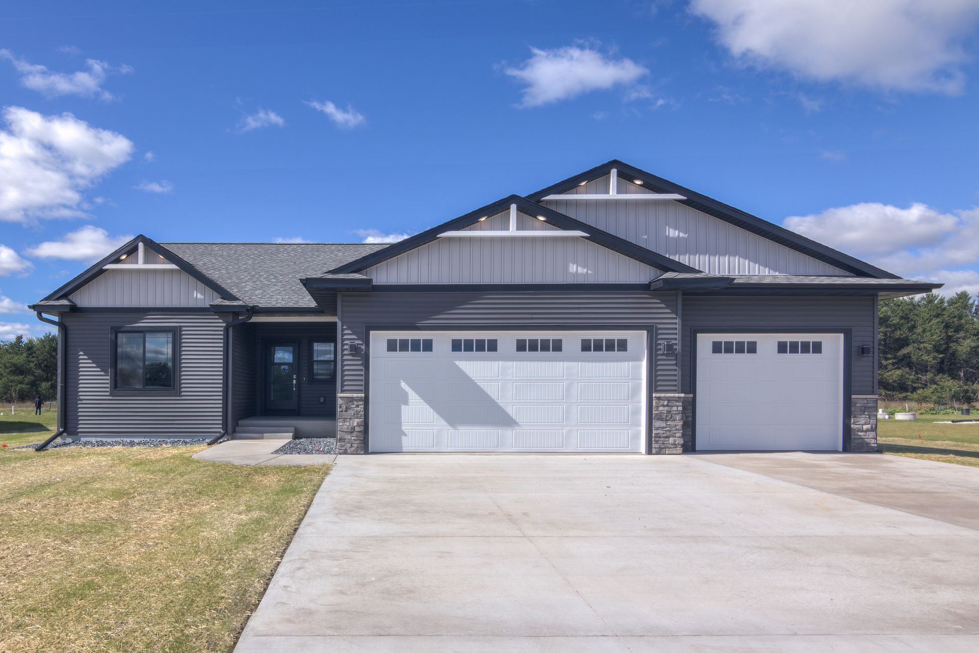 Modern gray house with white garage doors and concrete driveway under a blue sky.
