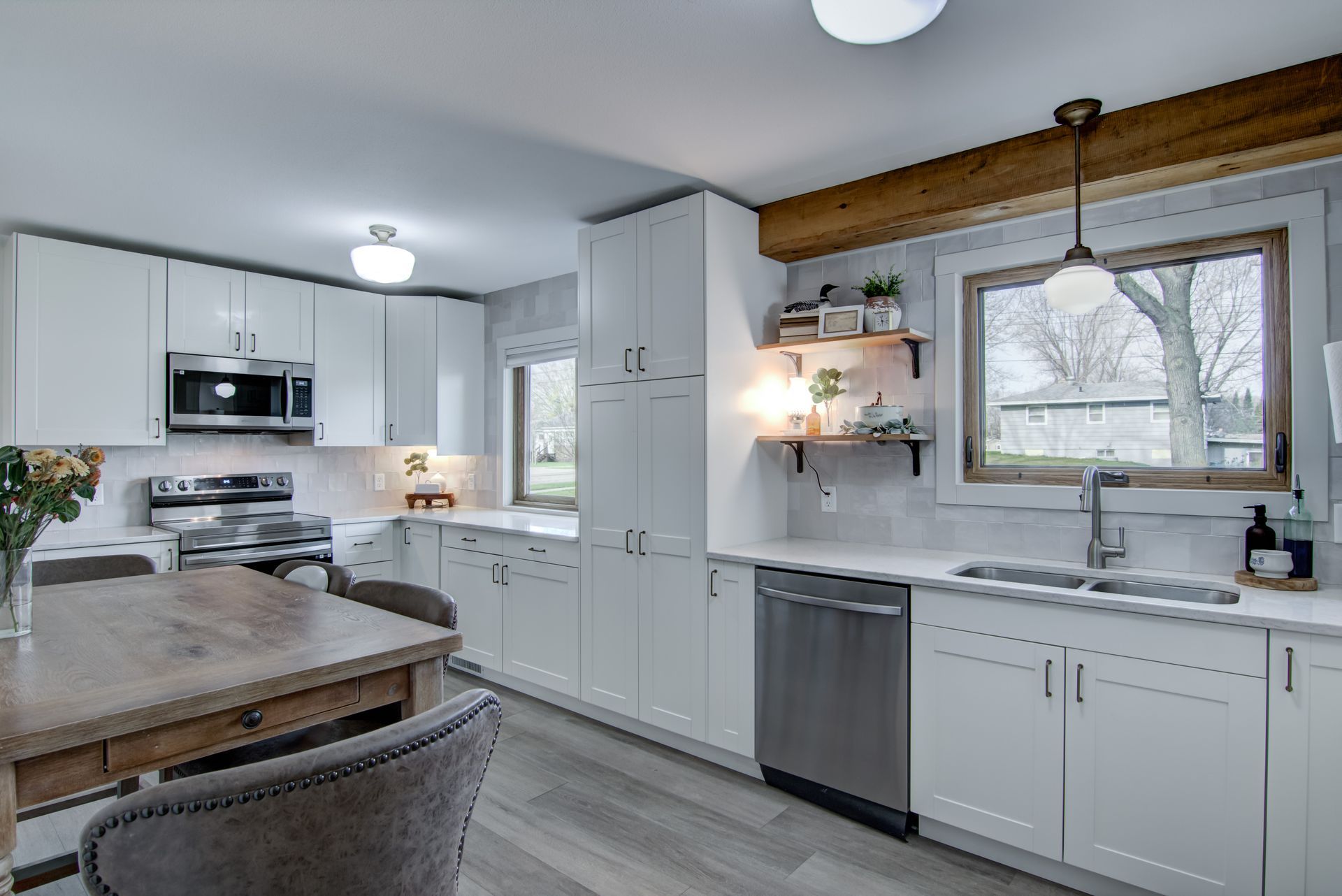 Modern white kitchen with stainless steel appliances, wood accents, and dining table.