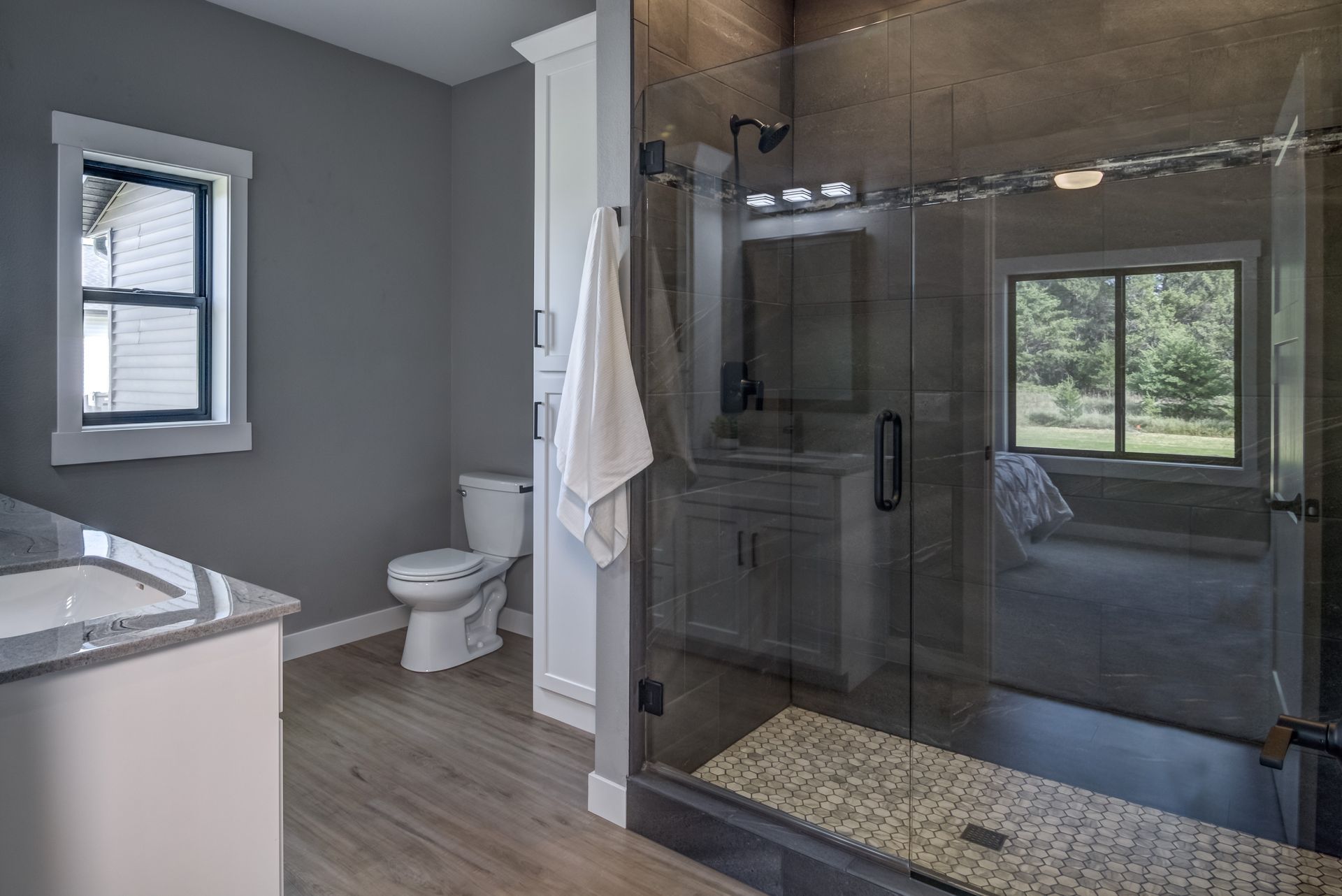 Modern bathroom with a glass shower, toilet, and vanity. Gray walls and wood-look flooring.