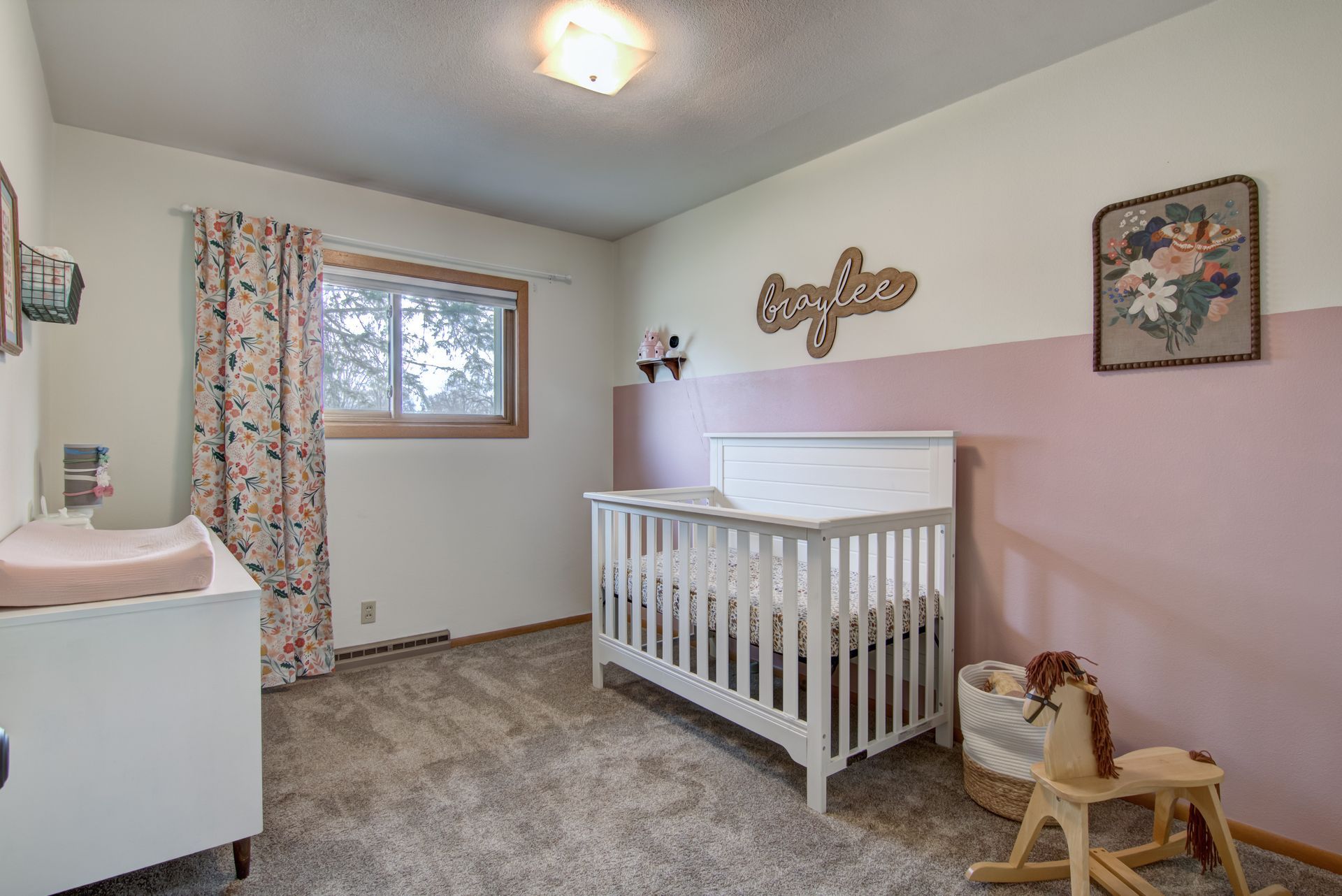 A nursery with a white crib, changing table, and pink and white walls.